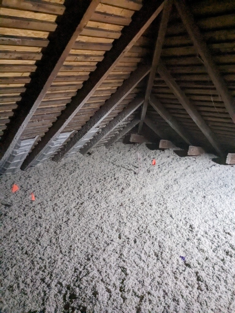 Attic floor covered in blown-in cellulose insulation with soffit baffles and depth marker flags