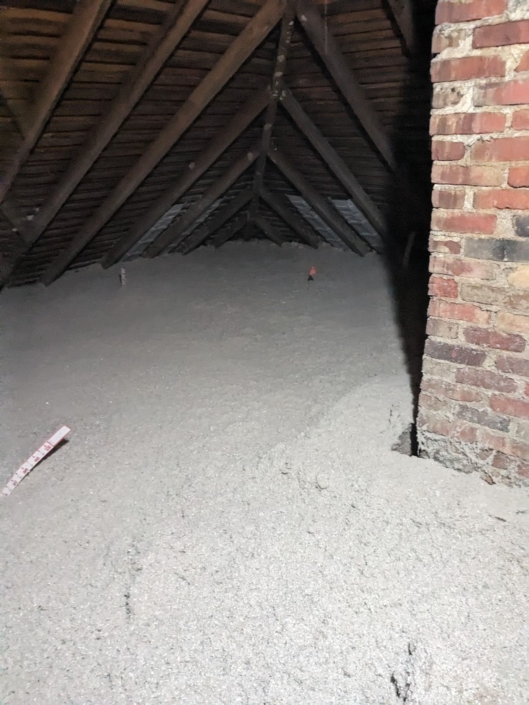 Finished blown-in attic insulation packed around a brick chimney with a depth ruler