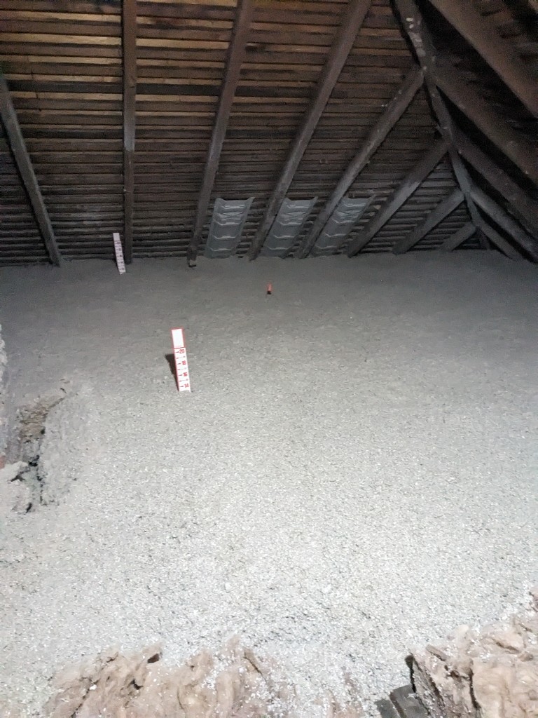 Attic blown-in insulation with depth gauges showing approximately 14 to 16 inches of coverage