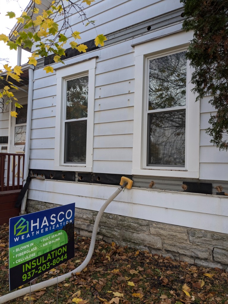Insulation blow hose filling wall cavities after a row of siding was removed