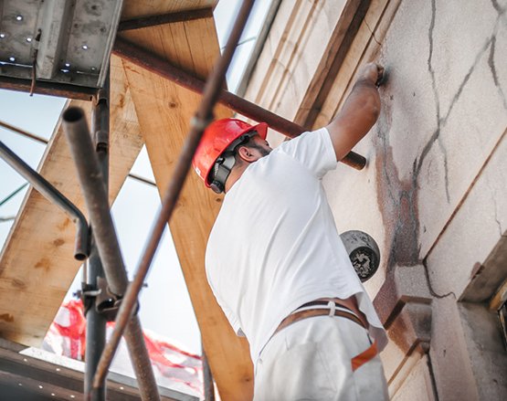 Worker in a red helmet repairing the exterior of a building using scaffolding.