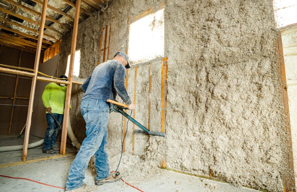 Workers installing cellulose insulation in a wall frame during construction.