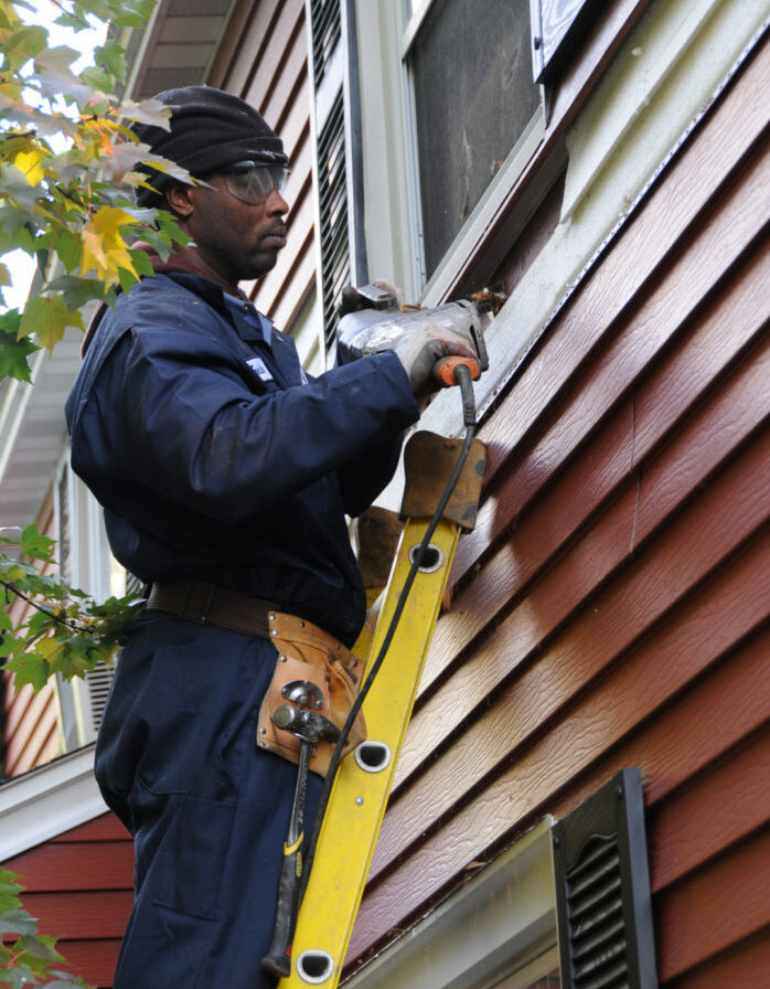 Worker installing insulation around a window on a ladder.